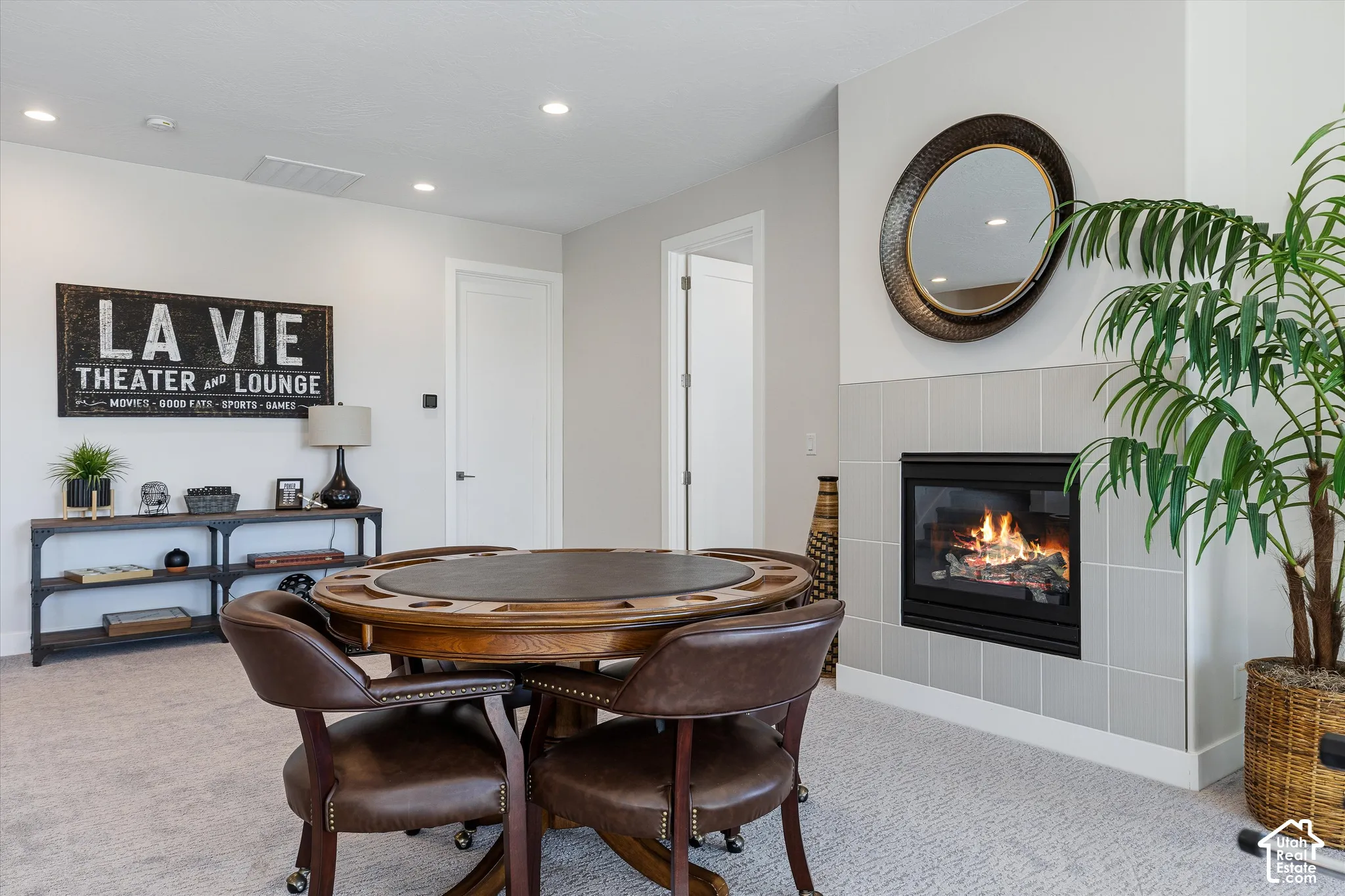 Recessed lighting, light gray wall tile surrounding a built-in fireplace, and a light-colored carpeted floor