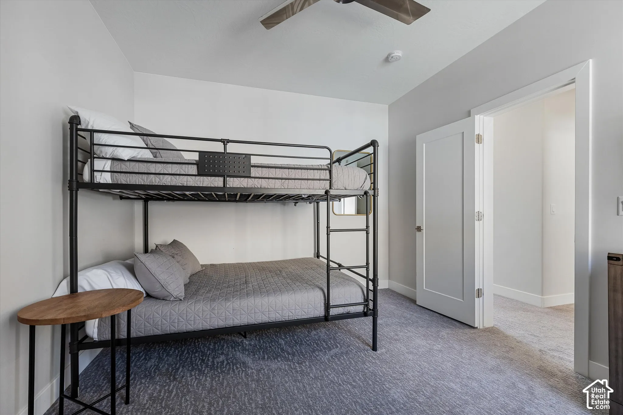 Light gray walls, light gray carpet flooring, white door, and a ceiling fan