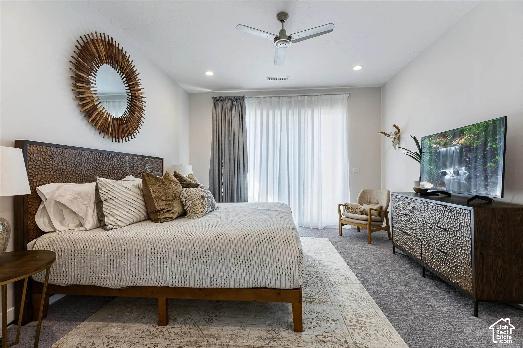 Neutral wall paint with recessed lighting, wood-finish headboard, built-in ceiling fan, light-filtering window treatments, and carpeted flooring