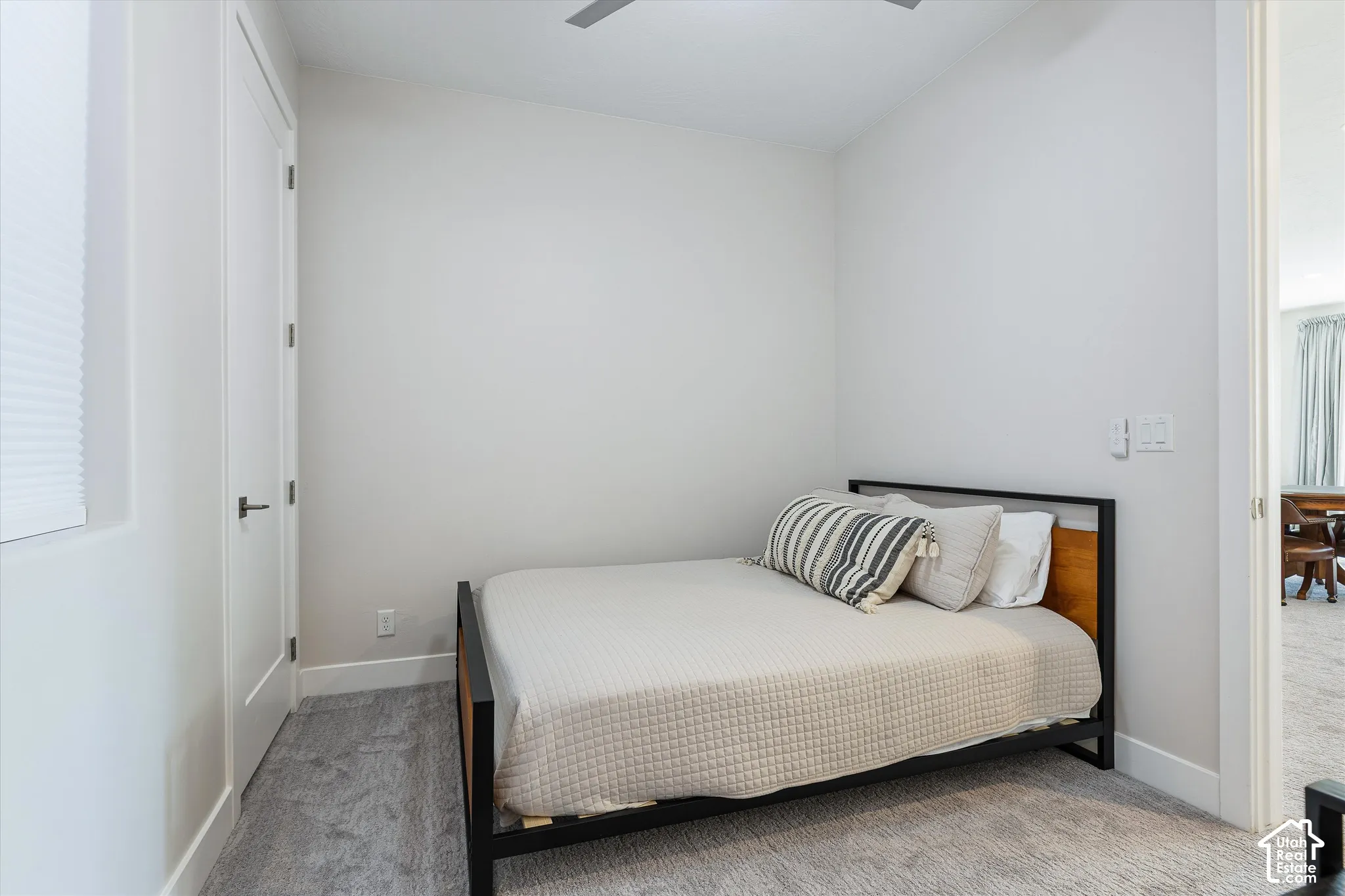 Neutral wall tones, gray carpeting, a flat-panel interior door with matte black hardware, and a window with a cellular shade