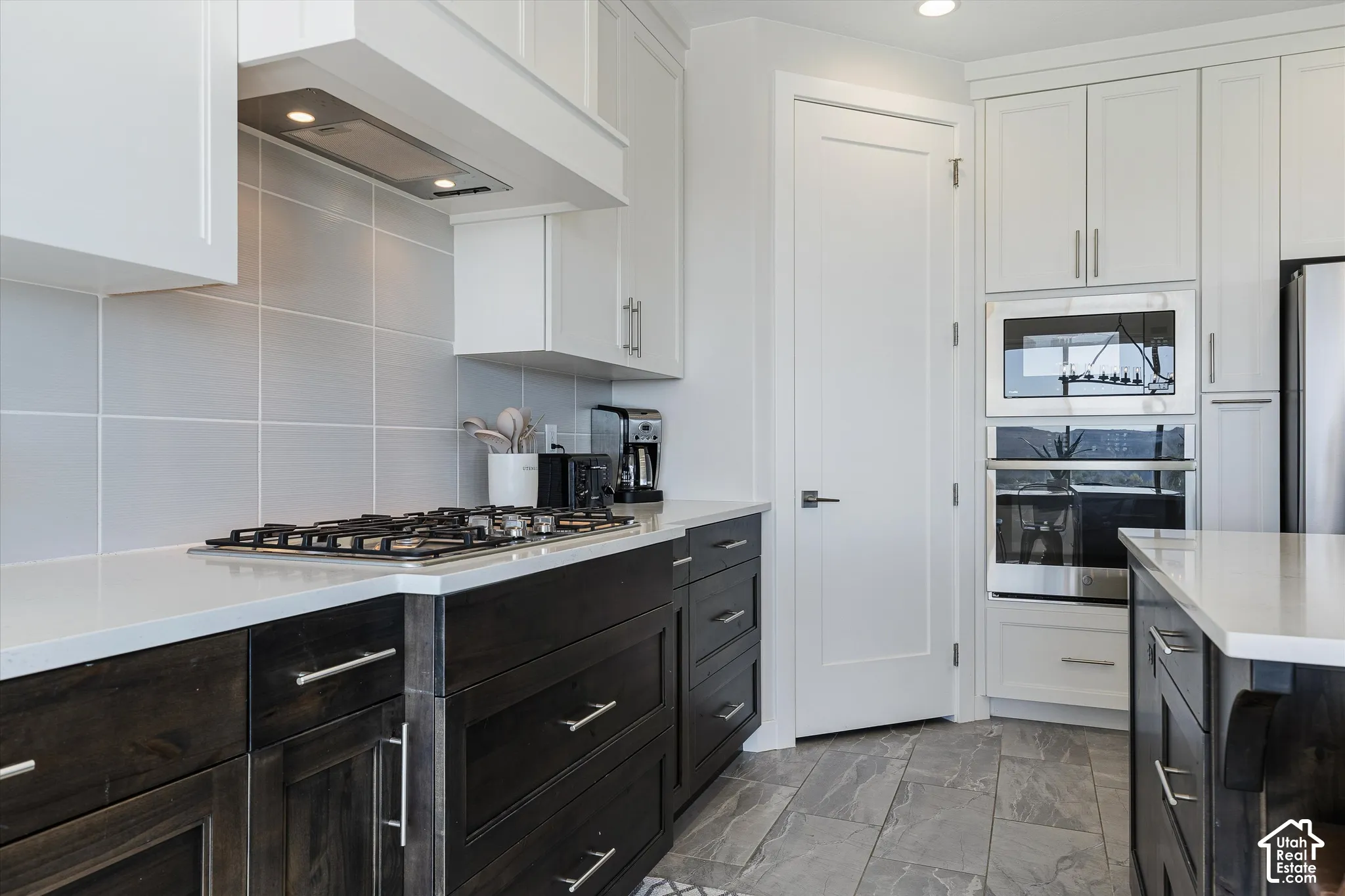 Kitchen featuring white upper cabinetry, dark wood-finish lower cabinetry, light-toned countertops, tile flooring, and stainless steel appliances