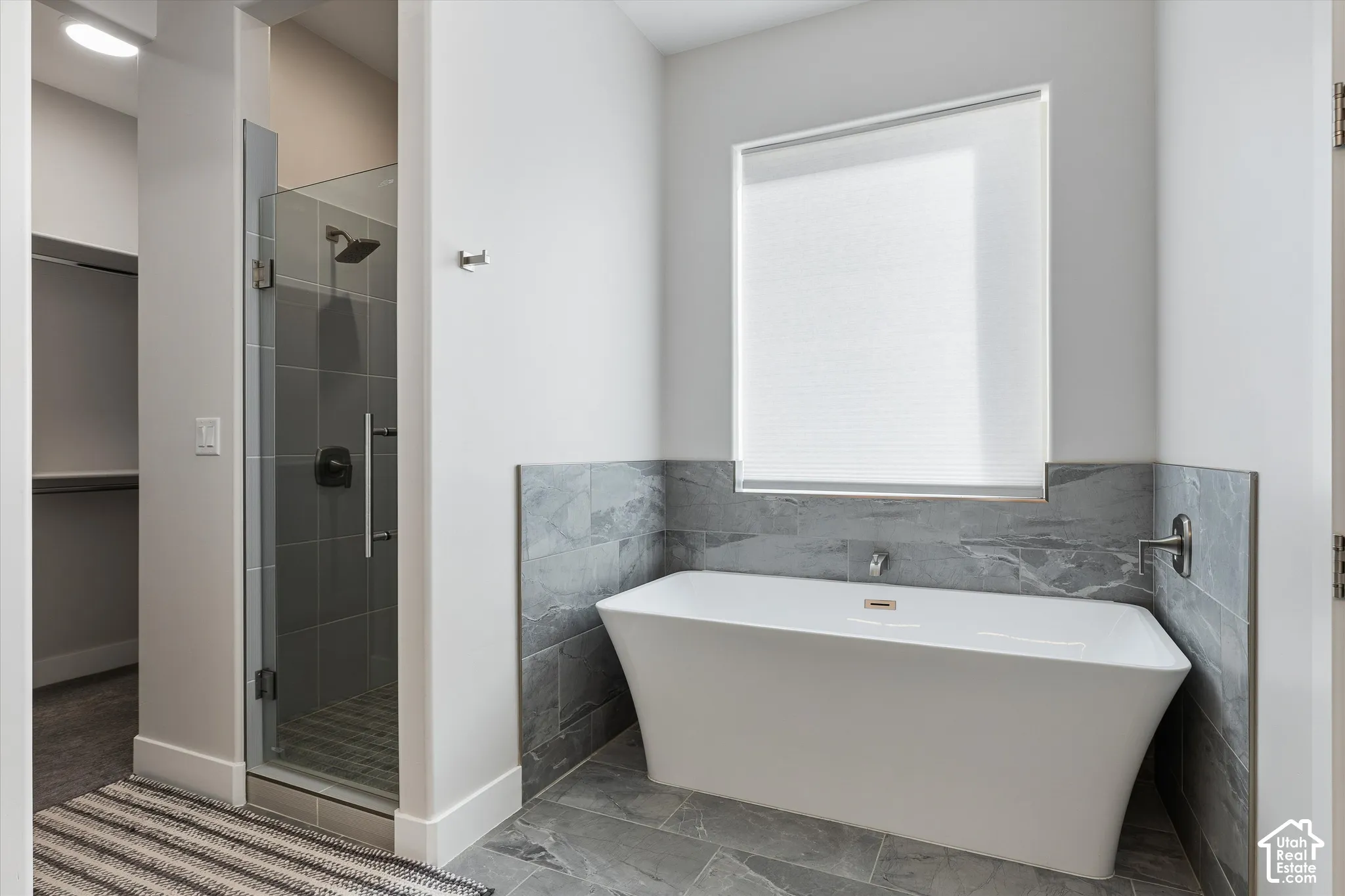 Freestanding soaking tub with a tiled surround, glass-enclosed shower with dark tile, and large format gray floor tile
