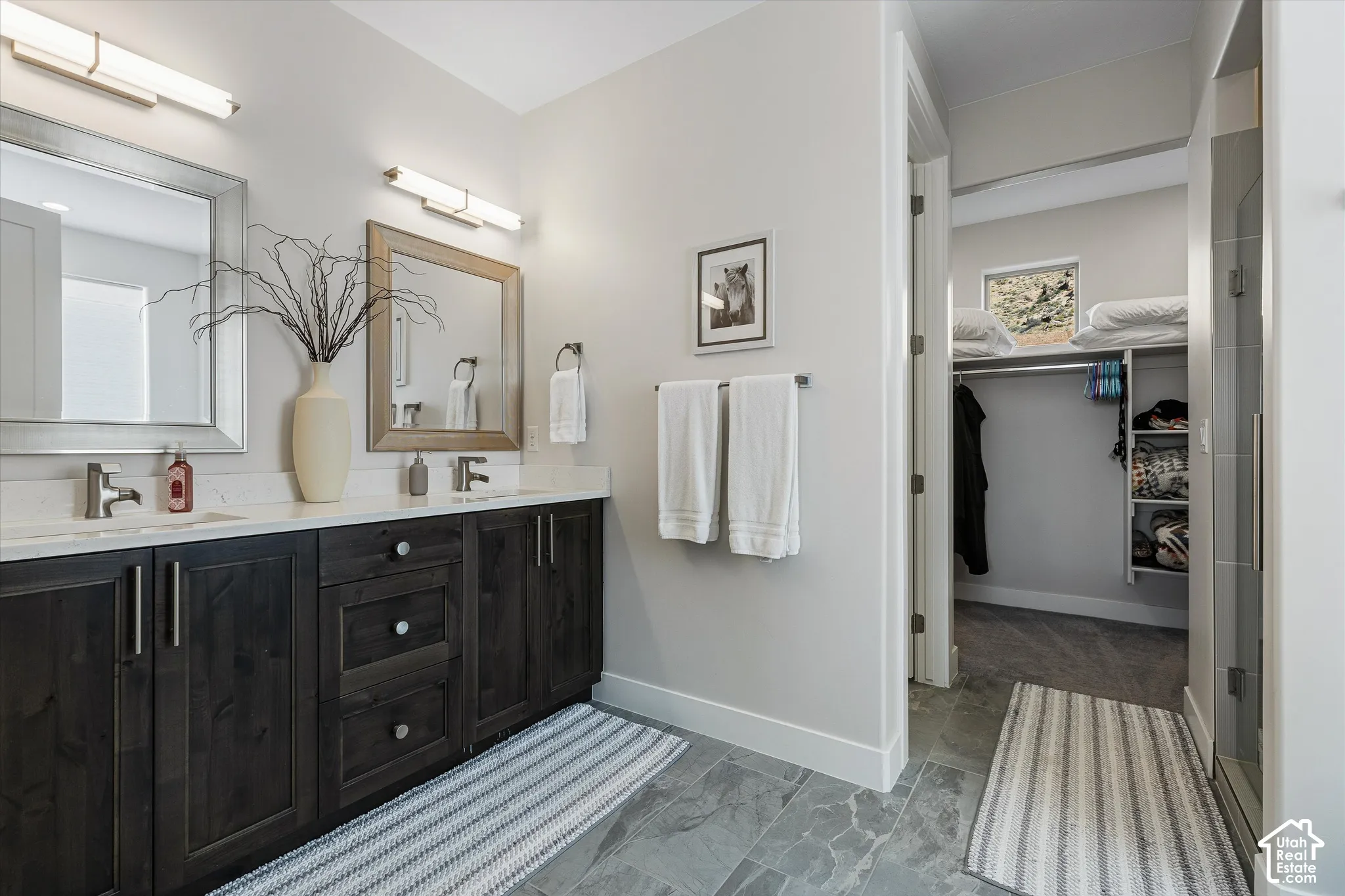 Dual sink vanity with dark wood-finish cabinetry, light stone-finish countertop, and brushed nickel faucets
