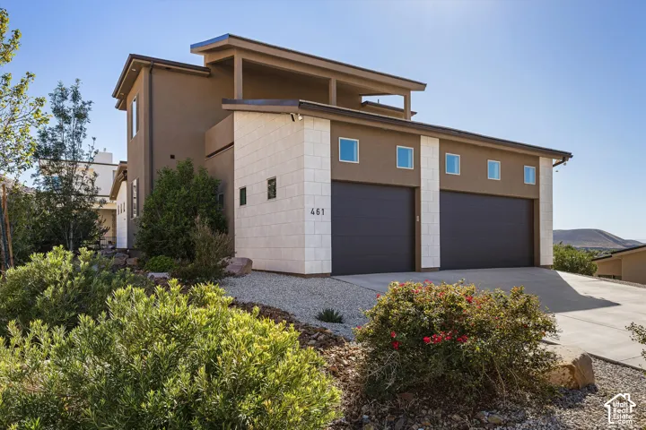 Contemporary exterior with stucco and stone accents, two dark garage doors, and a concrete driveway
