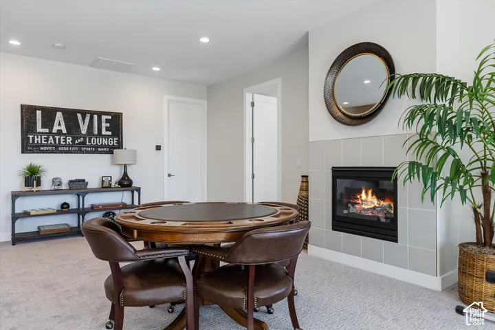 Recessed lighting, light gray wall tile surrounding a built-in fireplace, and a light-colored carpeted floor