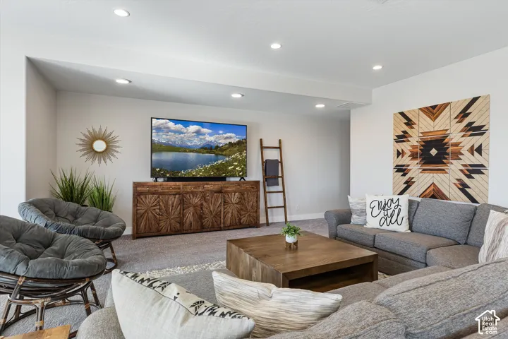Recessed lighting, wood-finish media console, and neutral wall tones complement the carpeted flooring