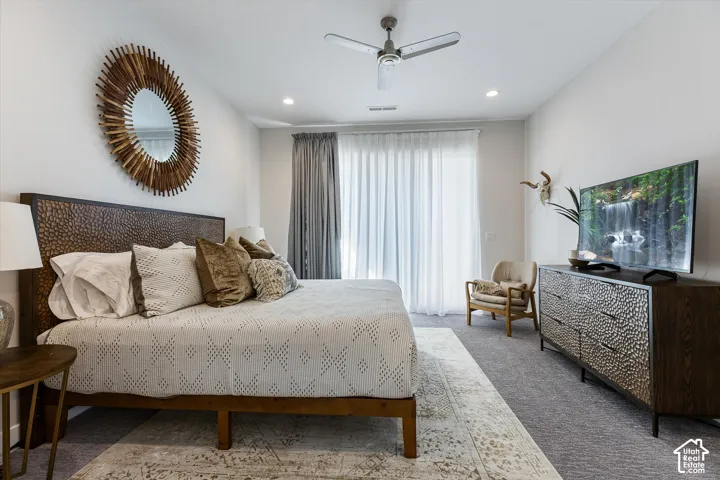 Neutral wall paint with recessed lighting, wood-finish headboard, built-in ceiling fan, light-filtering window treatments, and carpeted flooring