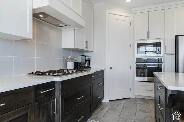 Kitchen featuring white upper cabinetry, dark wood-finish lower cabinetry, light-toned countertops, tile flooring, and stainless steel appliances