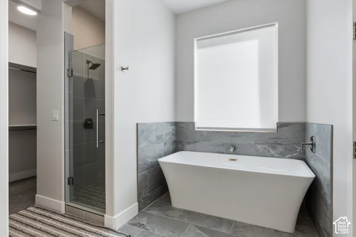 Freestanding soaking tub with a tiled surround, glass-enclosed shower with dark tile, and large format gray floor tile