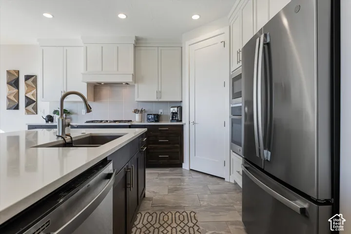 Kitchen featuring light cabinetry, dark wood-finish base cabinets, a stainless steel refrigerator, a built-in oven and microwave, and a kitchen island with an undermount sink