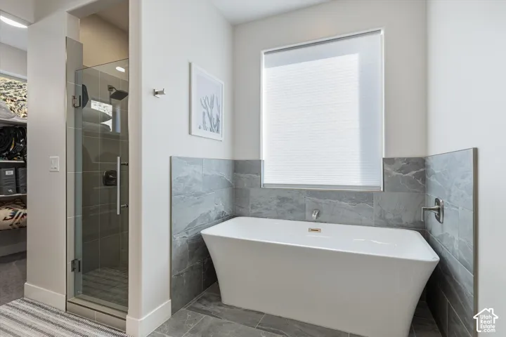 Freestanding tub with wall-mounted faucet, glass-enclosed shower with dark hardware, and large format grey tile flooring