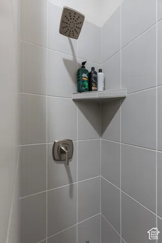 Rainfall showerhead with a brushed nickel finish, tiled shower walls, and a built-in corner shelf