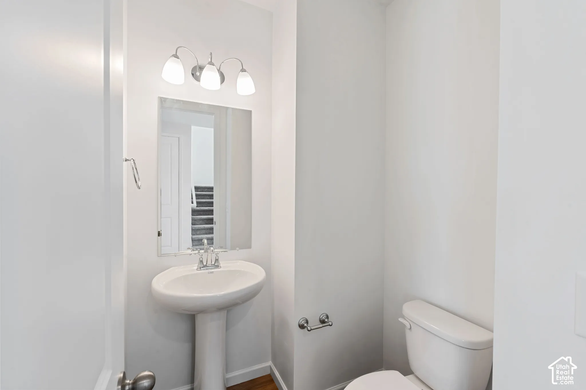 Pedestal sink with chrome faucet, mirror, wall-mounted light fixture, and white toilet. Picture from another model and for example only.