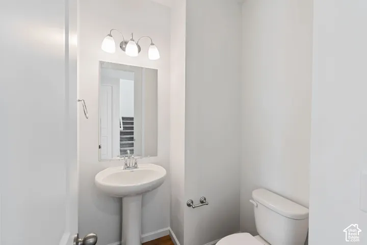 Pedestal sink with chrome faucet, mirror, wall-mounted light fixture, and white toilet. Picture from another model and for example only.