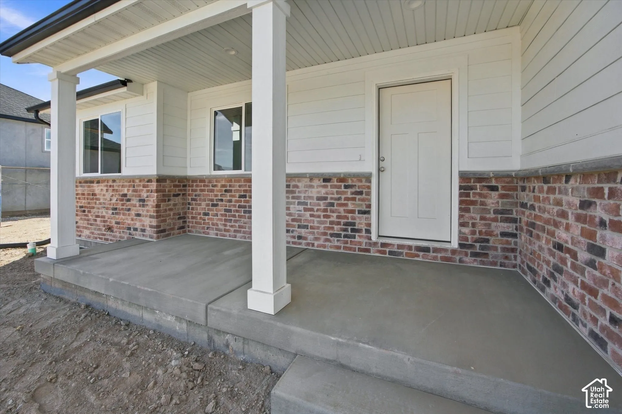 Covered concrete porch with white support columns, white siding, and brick veneer detailing