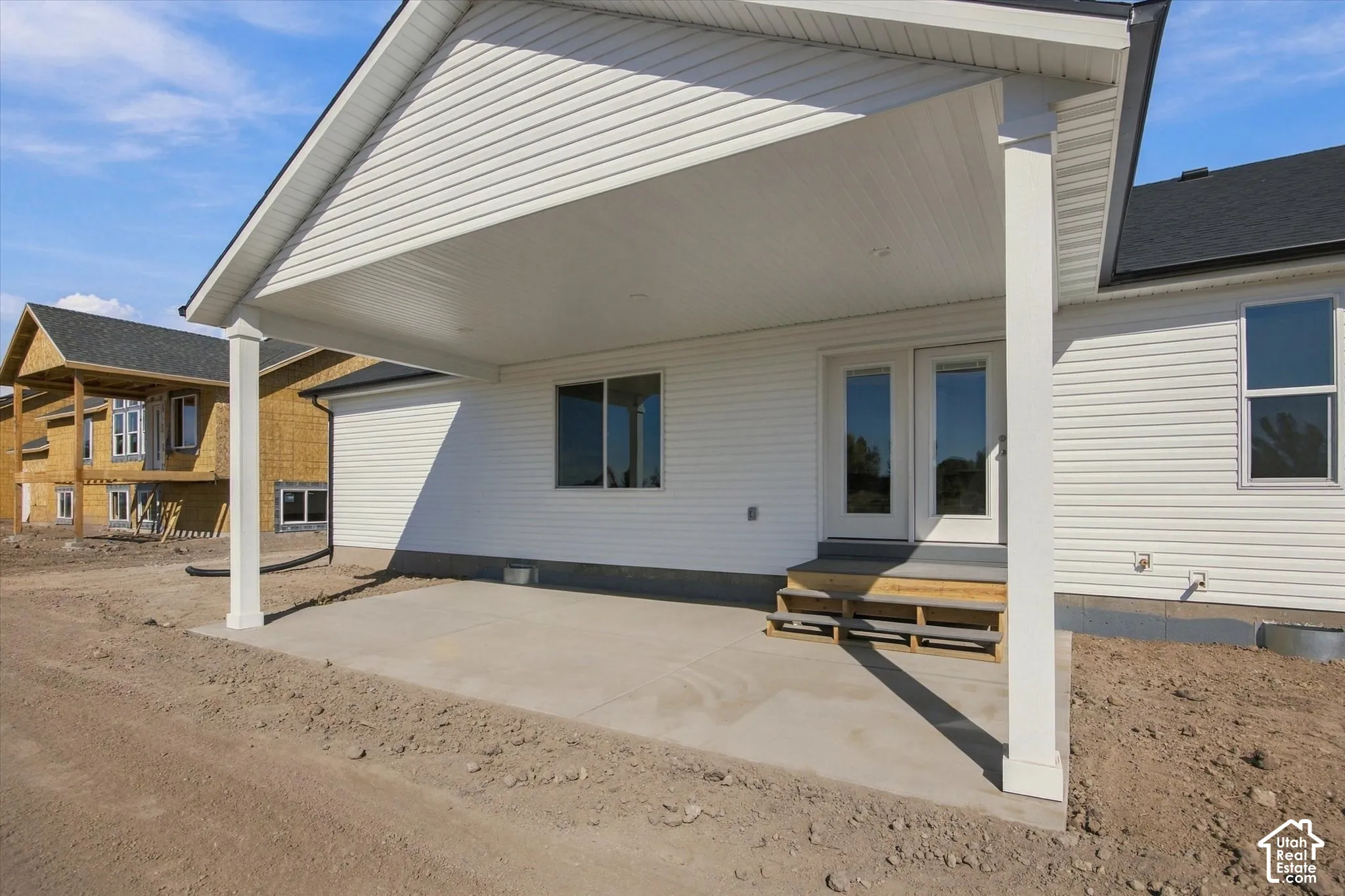 Covered concrete patio with recessed lighting, double-pane glass doors, and white vinyl siding