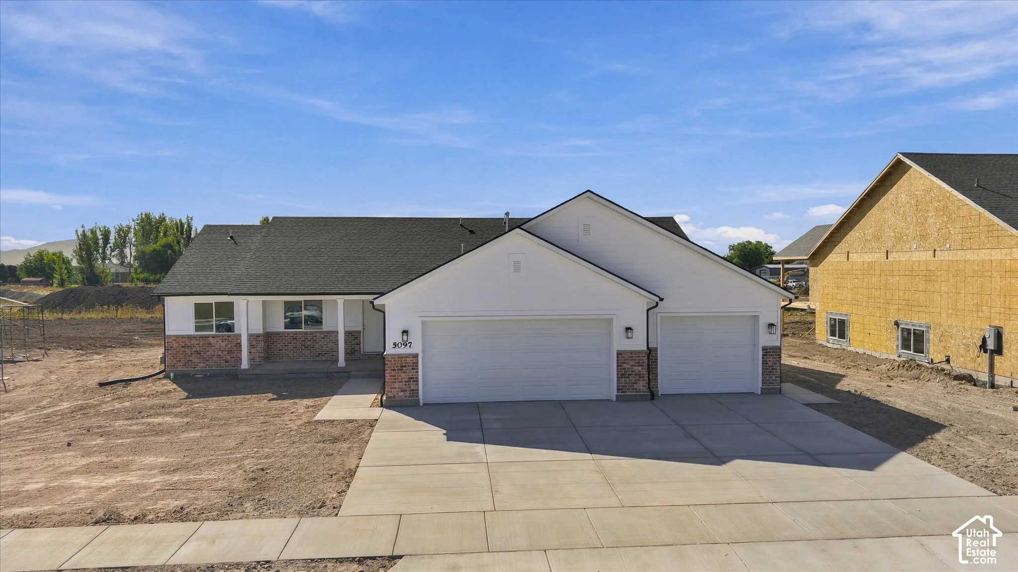White exterior with stone accents, covered front porch, two-car garage, and dark-pitched roof