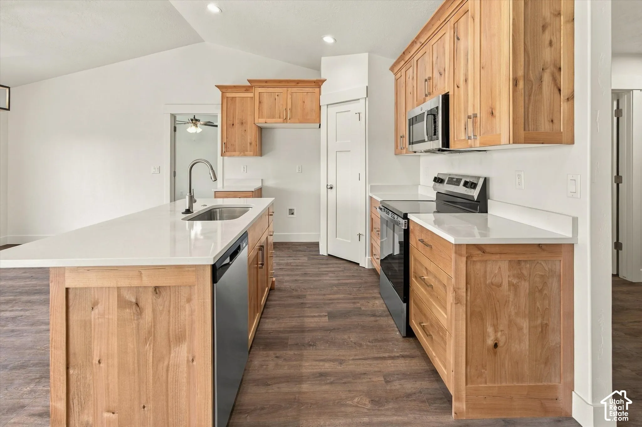 Kitchen featuring wood cabinetry, stainless steel appliances, white countertops, and an island with an undermount sink