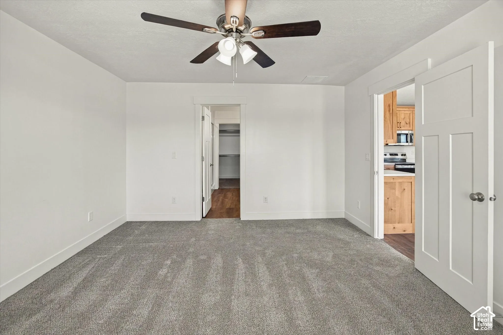 Gray carpeted flooring, white walls, and a ceiling fan with light fixture