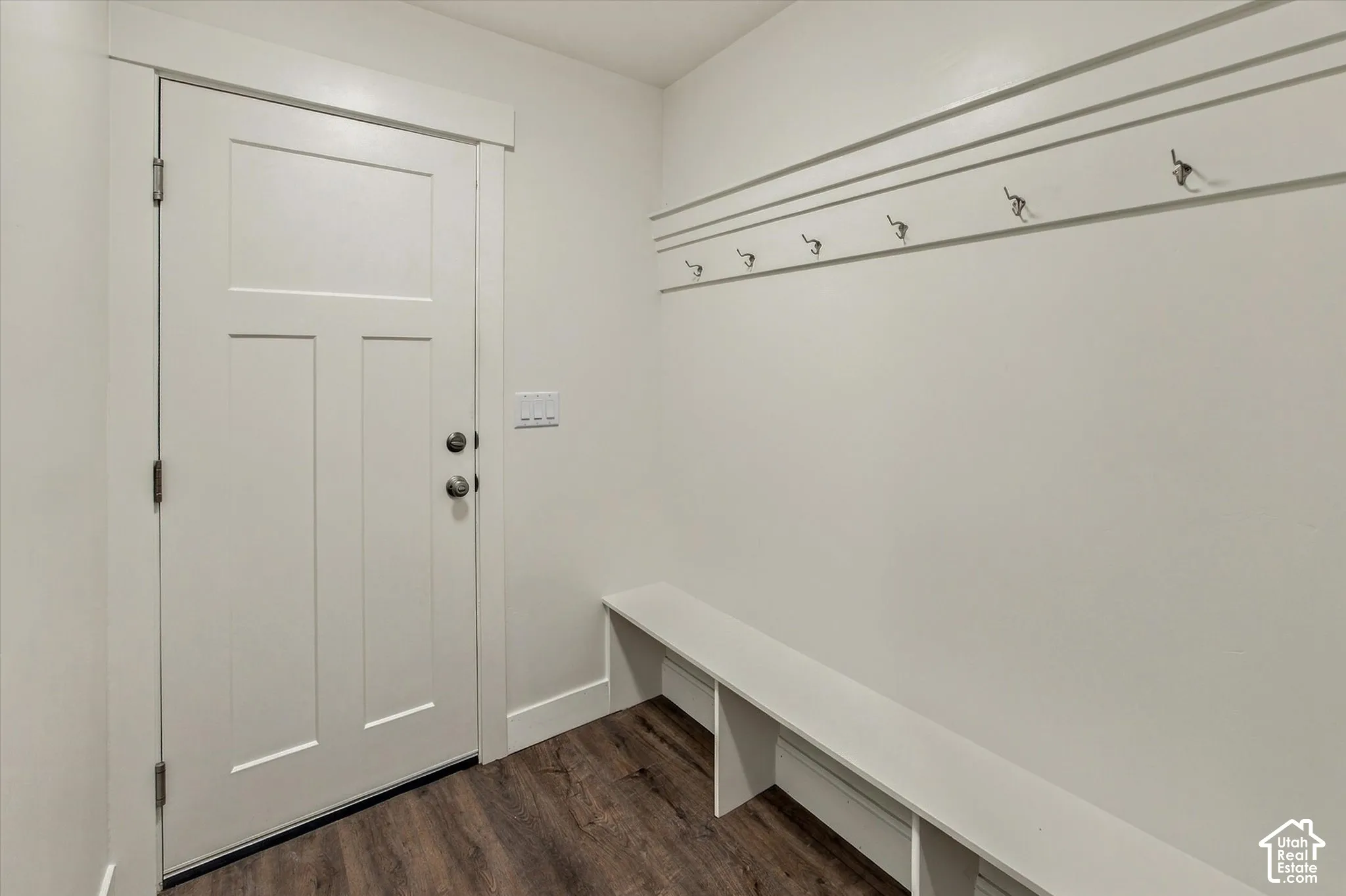 White paneled door with brushed nickel hardware, wood-finish flooring, built-in shelving, and wall-mounted coat hooks