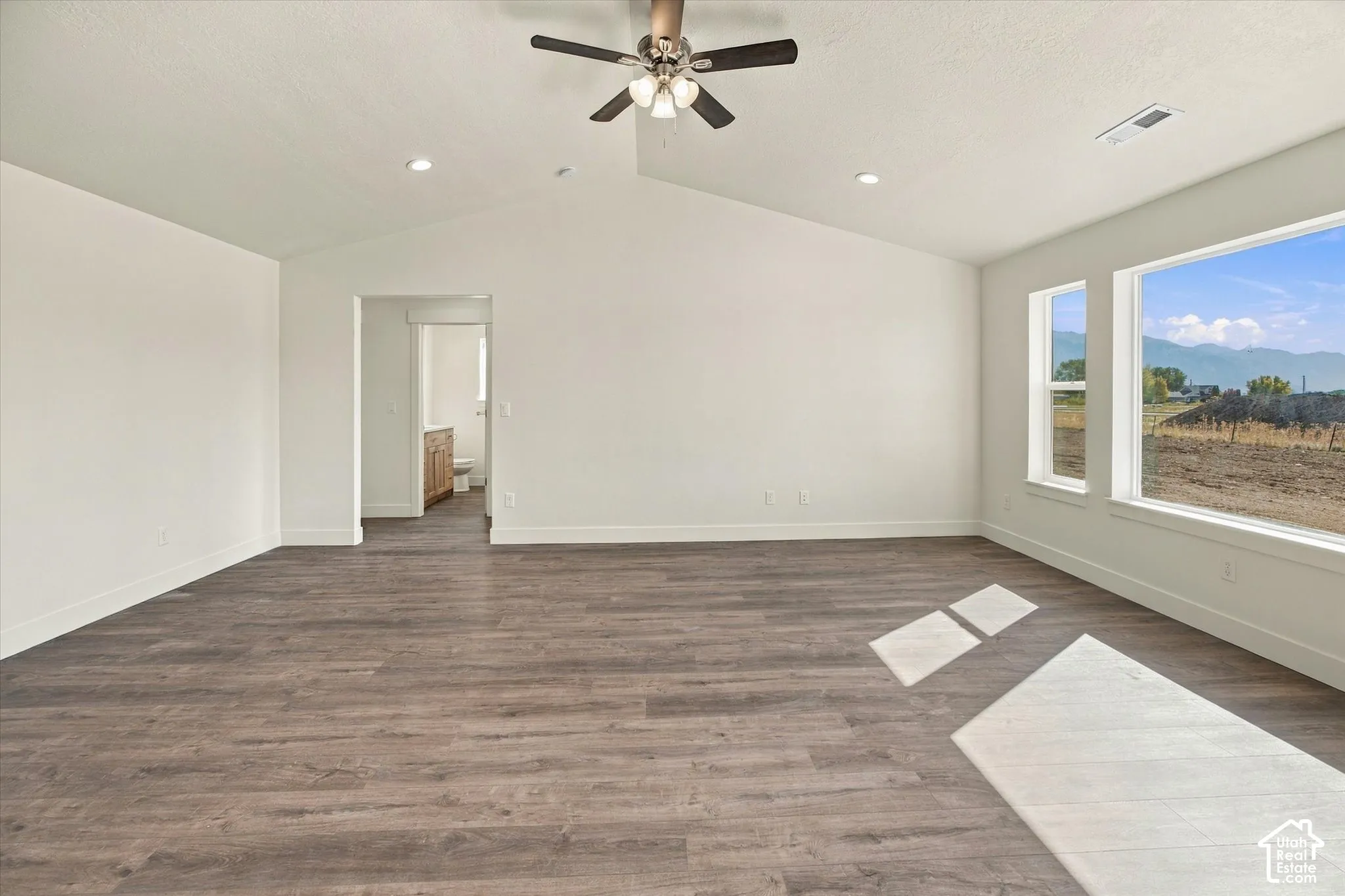 Spacious room featuring wood-finish flooring, vaulted ceiling, recessed lighting, ceiling fan, and large windows with mountain scenery