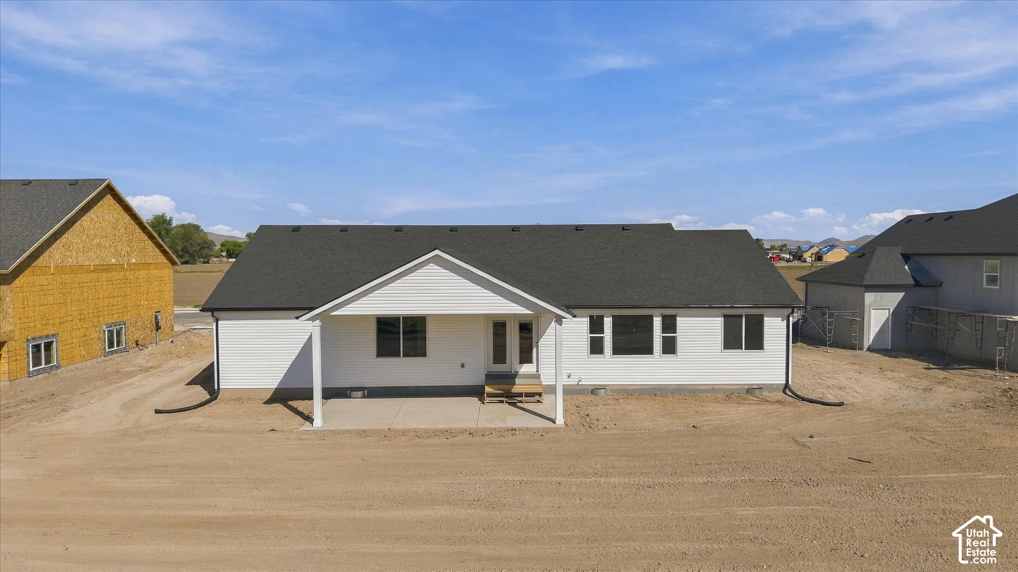 White siding exterior with a covered patio, dark shingle roof, and multiple windows
