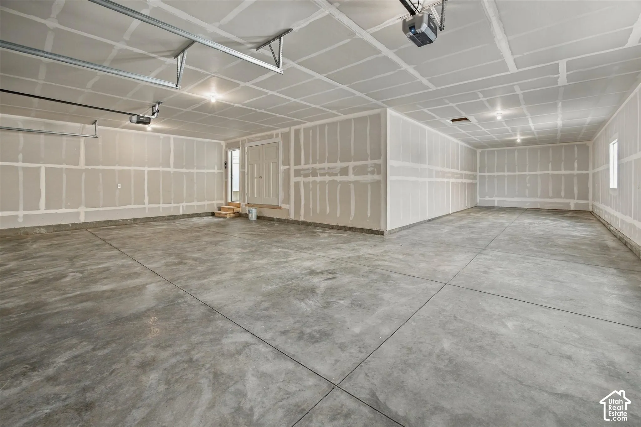 Expansive garage space featuring a concrete floor, high ceilings, multiple light fixtures, and a side entry door