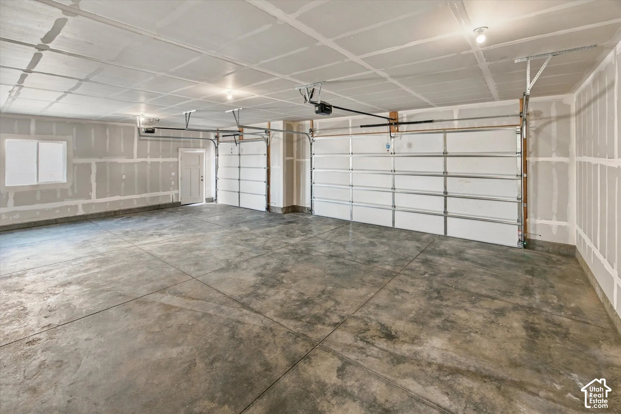Expansive garage with concrete flooring, two overhead doors, a window, and an interior access door