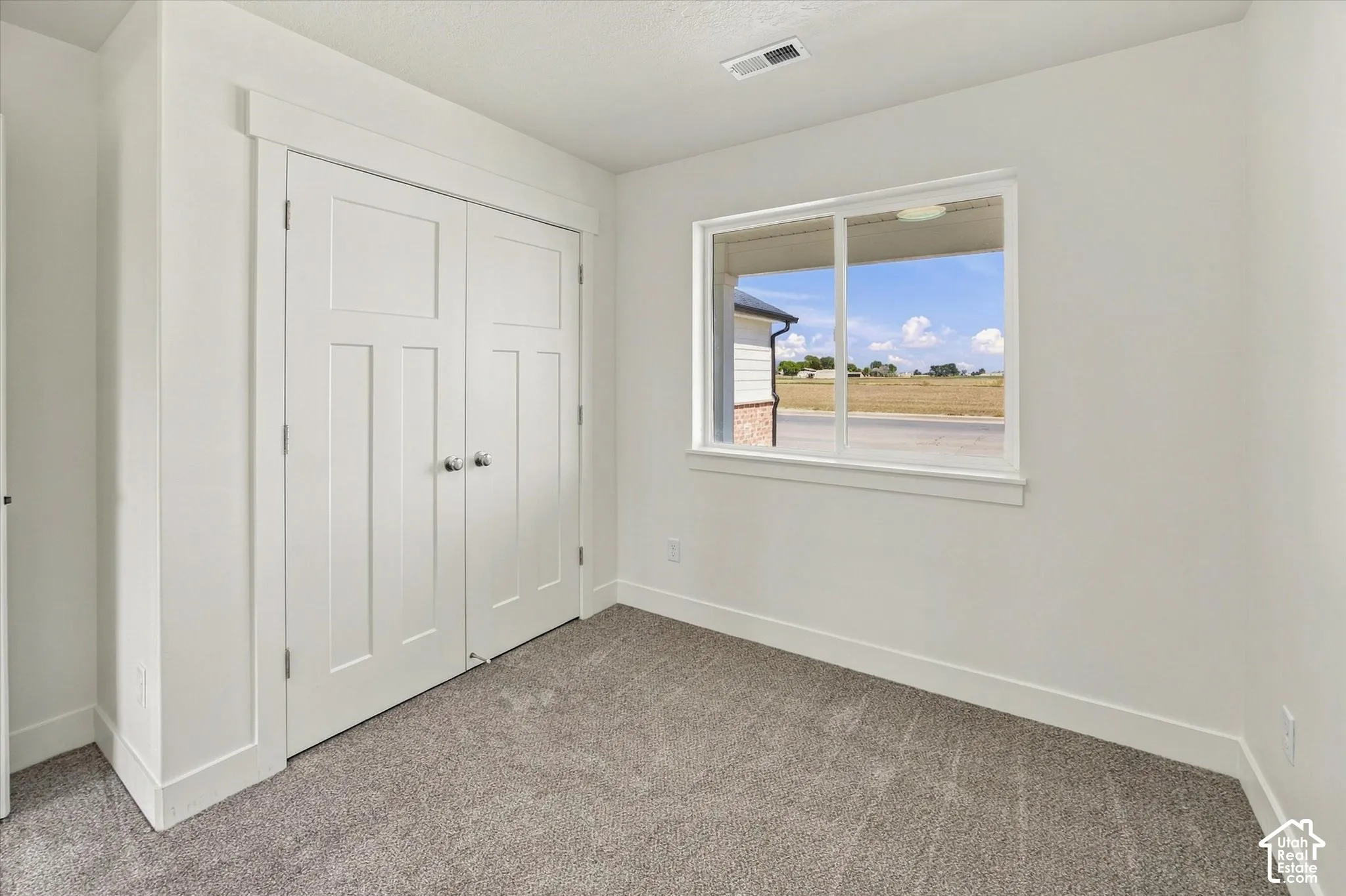Crisp white walls with clean-lined trim, a double-door closet with polished hardware, a bright window, and plush carpeting