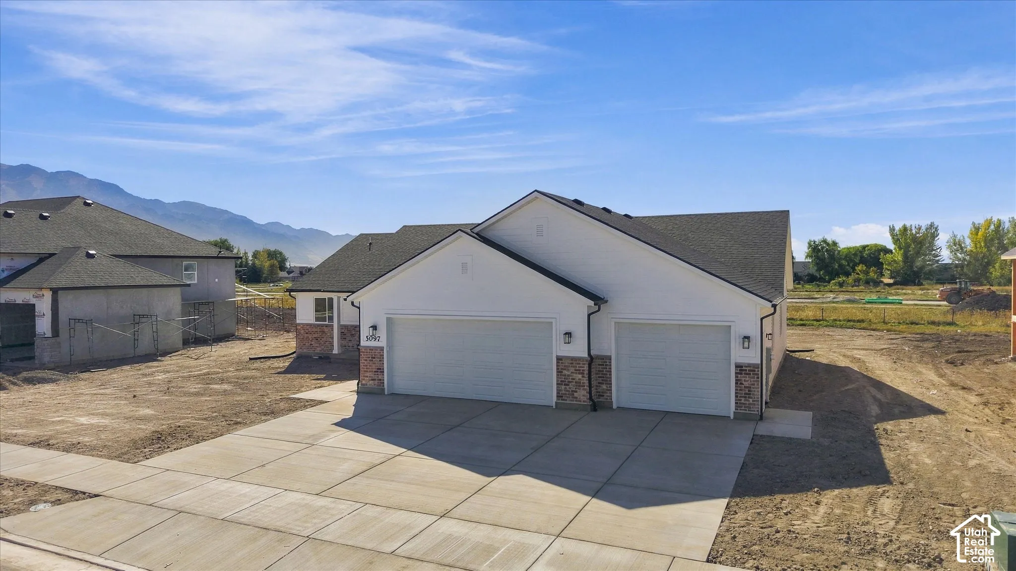 Contemporary exterior with white siding and brick accents, featuring two garage doors, a concrete driveway, and dark shingle roofing