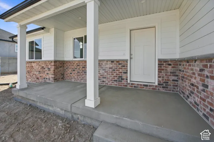 Covered concrete porch with white support columns, white siding, and brick veneer detailing