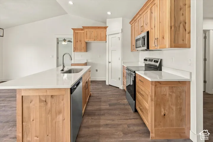 Kitchen featuring wood cabinetry, stainless steel appliances, white countertops, and an island with an undermount sink