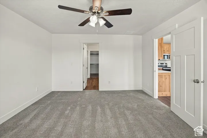 Gray carpeted flooring, white walls, and a ceiling fan with light fixture