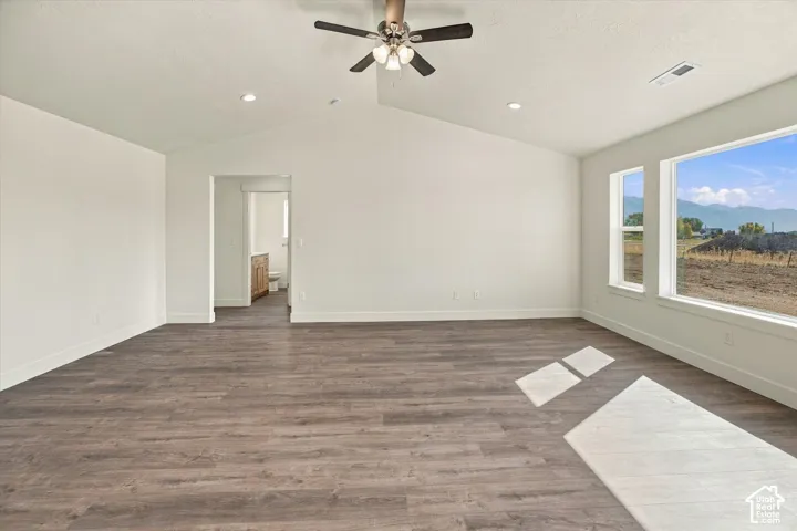 Spacious room featuring wood-finish flooring, vaulted ceiling, recessed lighting, ceiling fan, and large windows with mountain scenery