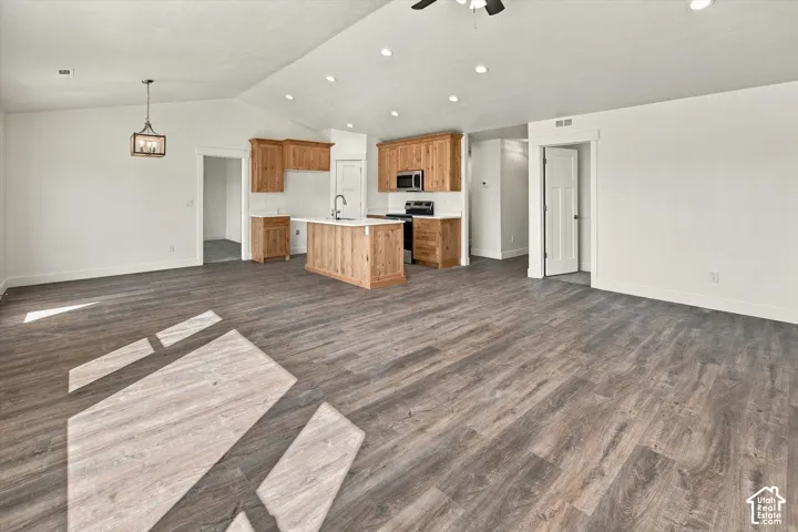 Vaulted ceilings with recessed lighting, wood-finish flooring, wood cabinetry, and a kitchen island with a sink