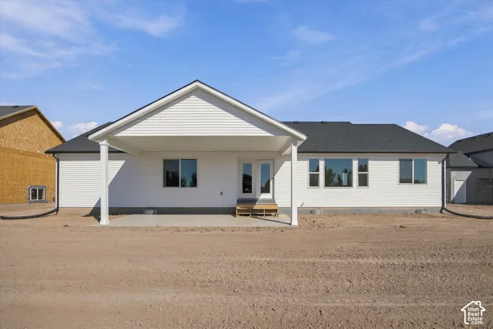 White siding exterior with a covered patio, multiple windows, and a dark shingle roof
