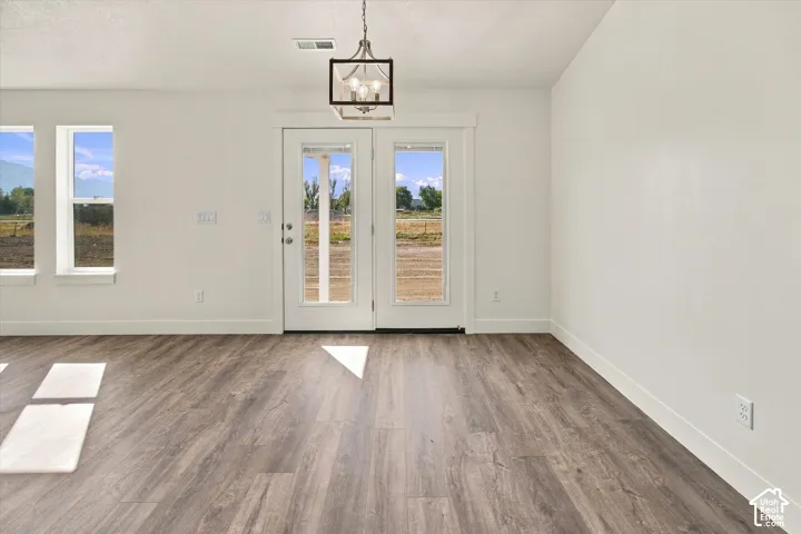 Wood-finish flooring with white baseboards, bright white walls, and a contemporary chandelier