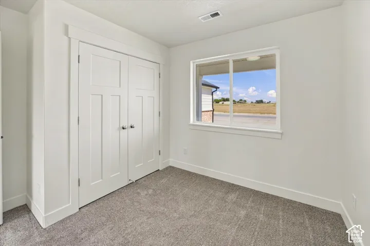 Crisp white walls with clean-lined trim, a double-door closet with polished hardware, a bright window, and plush carpeting