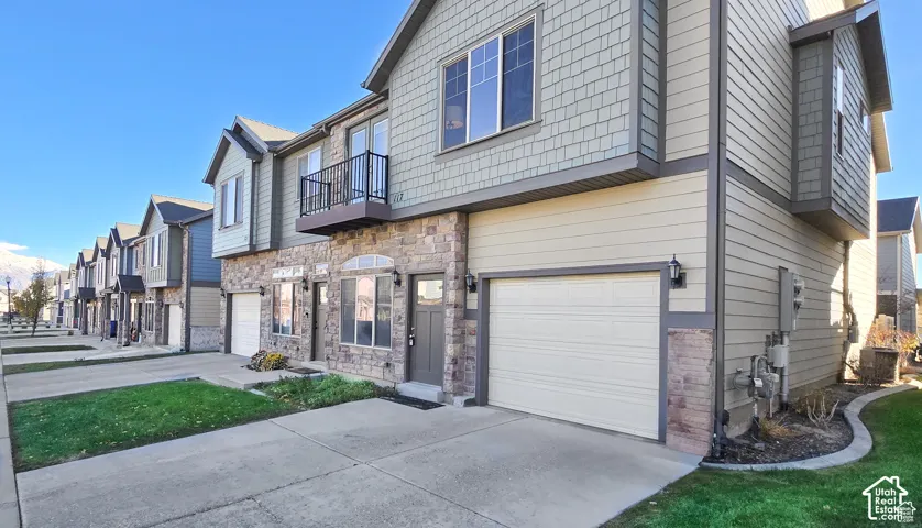 Stone and siding exterior with an integrated garage, private balcony, and multiple windows