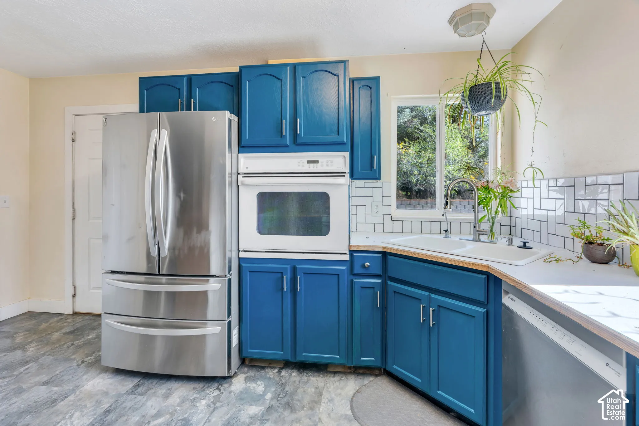 Kitchen featuring blue cabinetry, a stainless steel refrigerator, white wall oven, white subway tile backsplash, and wood-finish countertops