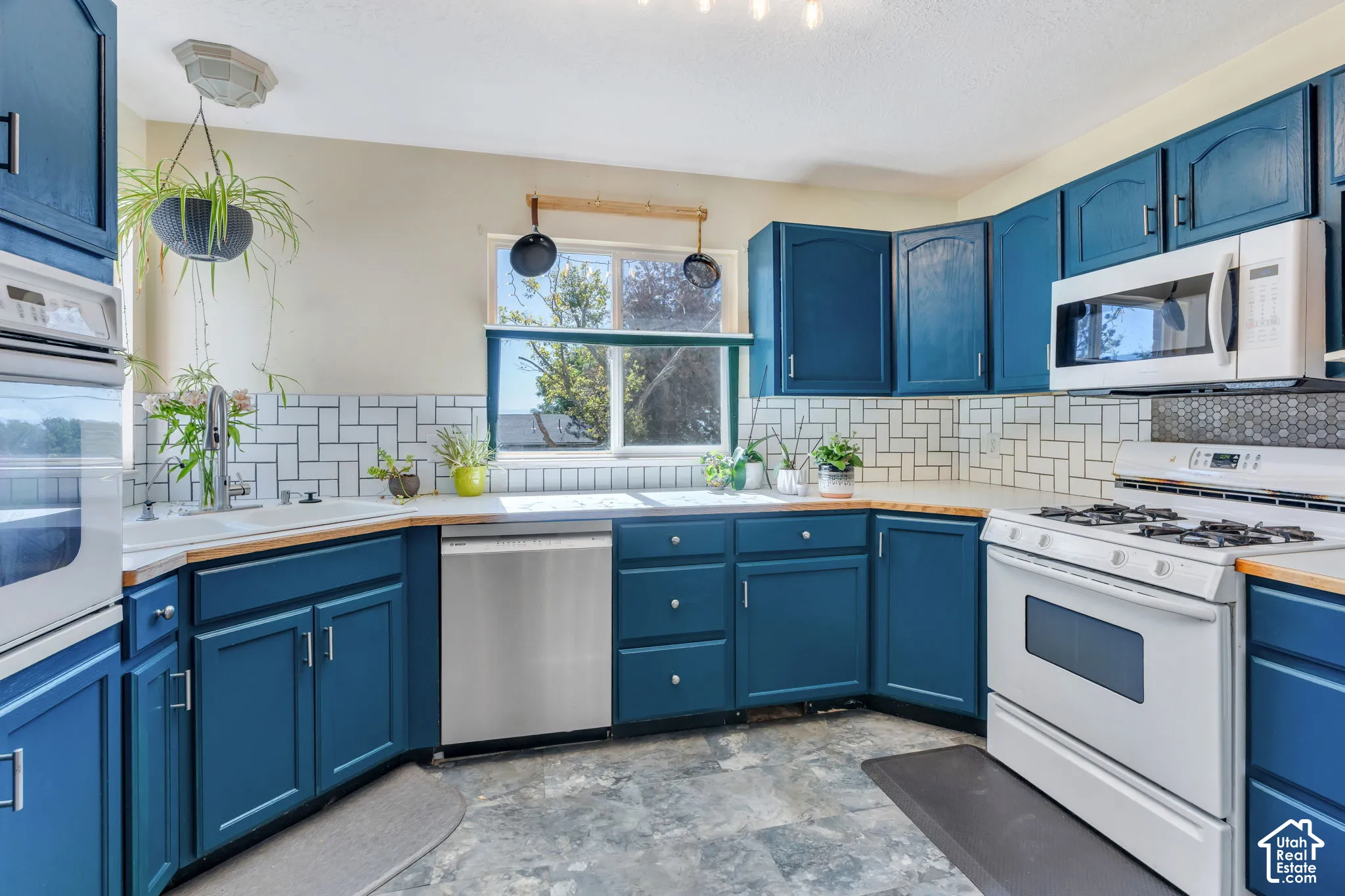 Kitchen featuring blue cabinetry, a white subway tile backsplash, a stainless steel dishwasher, and a white gas range