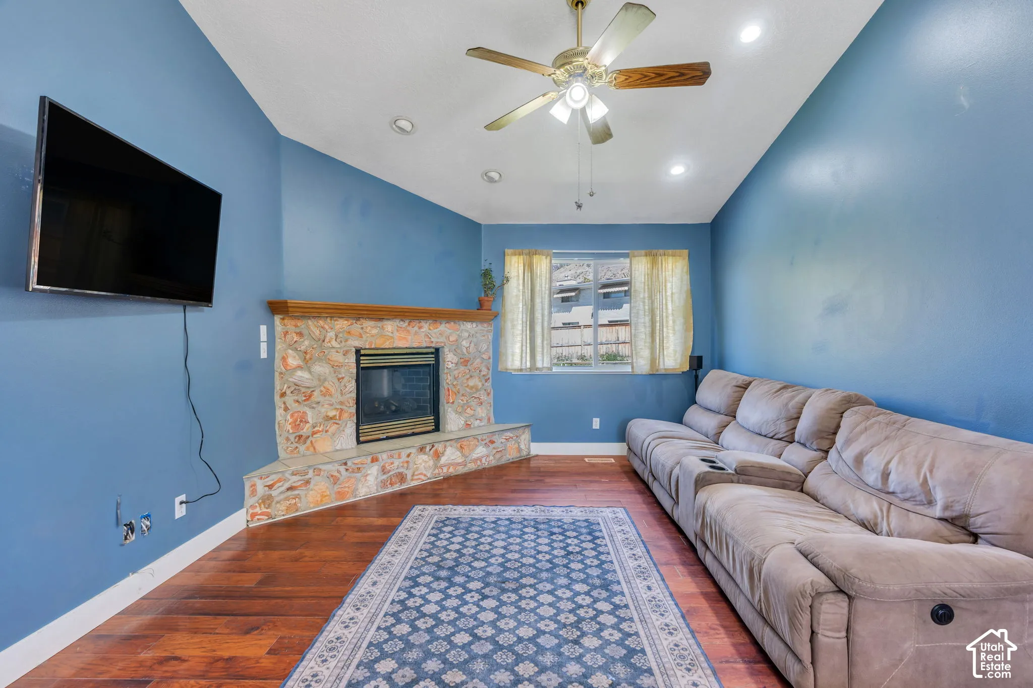 Vaulted ceiling with a ceiling fan, recessed lighting, wood-finish flooring, and a stone-faced fireplace with a wood mantle