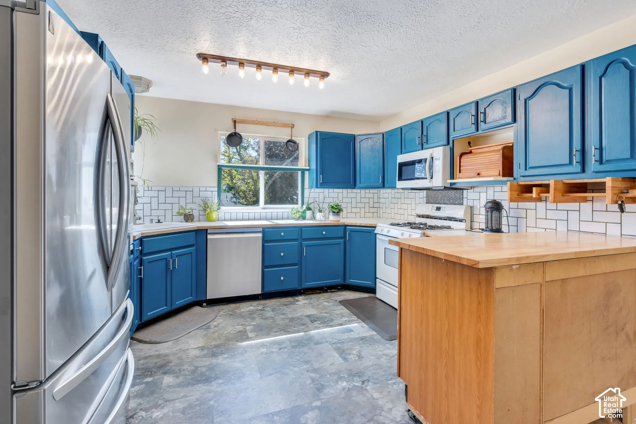 Kitchen featuring blue cabinetry, a white subway tile backsplash, a stainless steel dishwasher, a white gas range, and a wood-finish mobile island