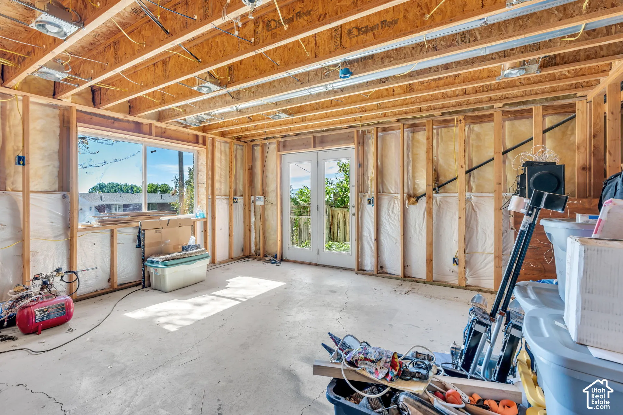 Exposed wood framing, concrete flooring, exterior window, and a door with glass panels