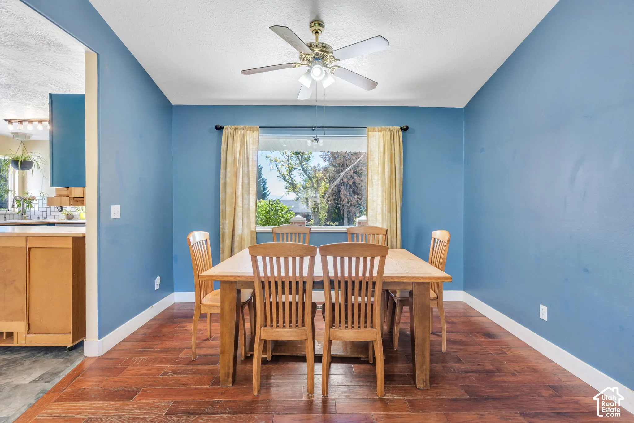 Wood-finish flooring with a ceiling fan light fixture and a window with curtains