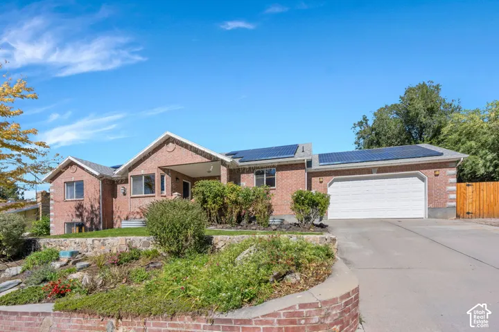 Brick exterior, solar panels, attached garage, concrete driveway, and tiered landscaping