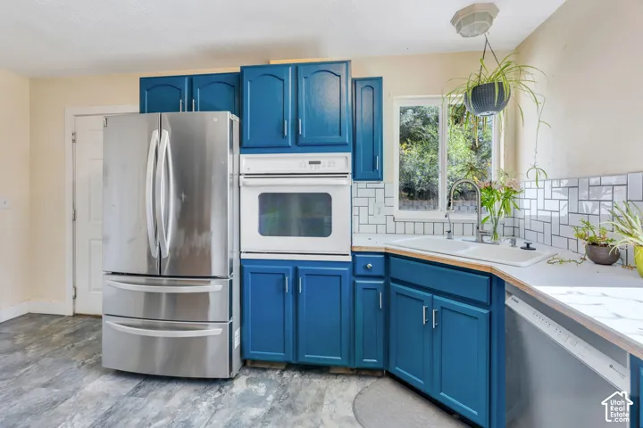 Kitchen featuring blue cabinetry, a stainless steel refrigerator, white wall oven, white subway tile backsplash, and wood-finish countertops