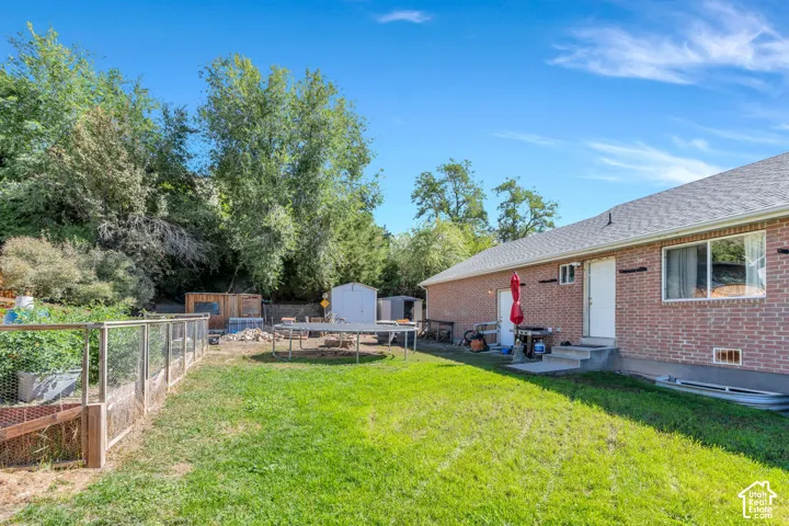 Expansive grassy yard with mature trees, a brick exterior, and a fenced garden area