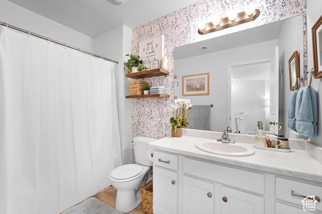 Vanity with white cabinetry and integrated sink, wall-mounted light fixture, full-width vanity mirror, and wood-finish flooring