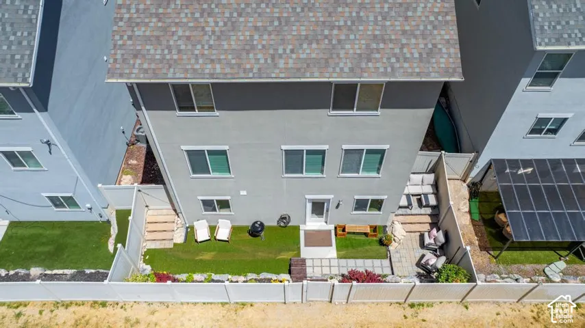 Rear exterior featuring a multi-level patio with pavers, artificial turf, and a white fence